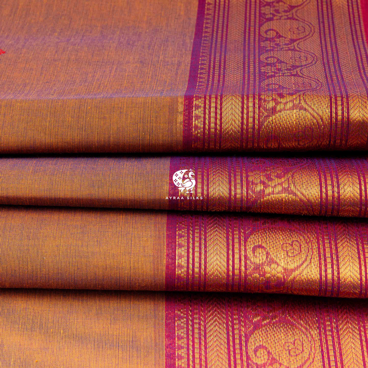 Folded rust cotton saree showing the magenta border with mankolam paisley in zari