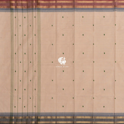 Beige cotton saree laid flat, green buttas and striped lines along the pallu and two Ganga Jamuna borders — maroon on one side, charcoal grey on the other