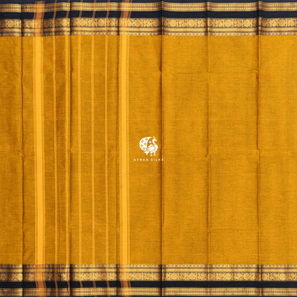 Mustard Kanchi cotton saree laid flat, pallu with stripes and the black and gold zari peacock border