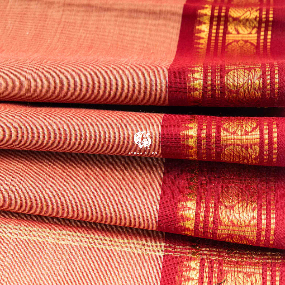 Folded stack showing the temple points where the brick red zari border meets the peach body