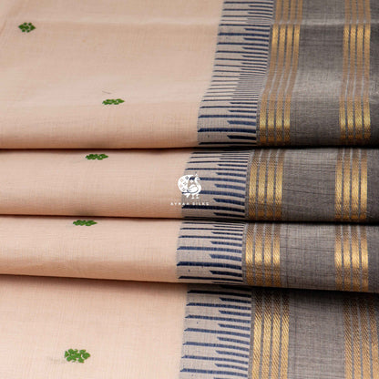 Folded beige cotton saree showing the charcoal grey border with gold zari lines