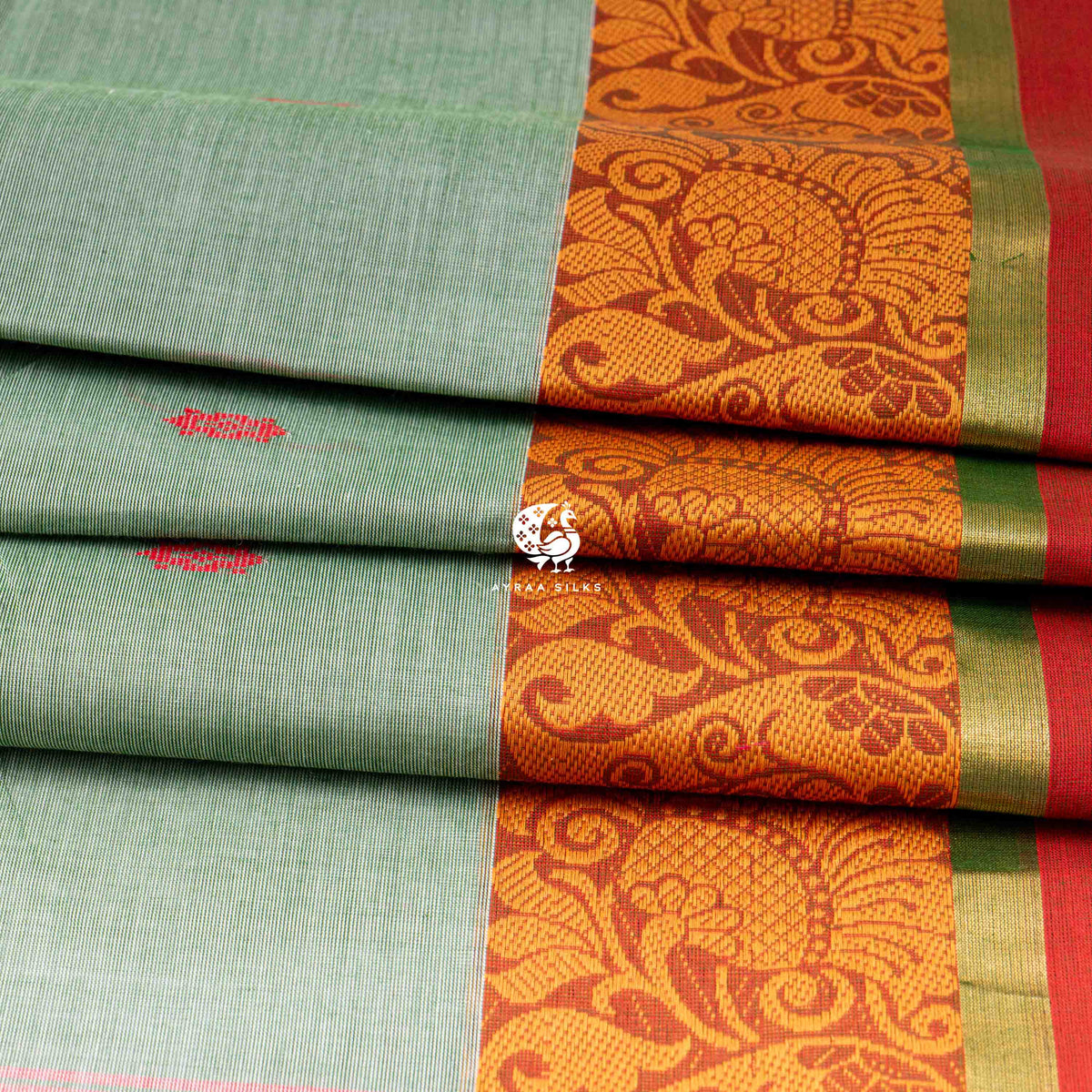 Folded sage green cotton saree showing the orange border with mankolam paisley