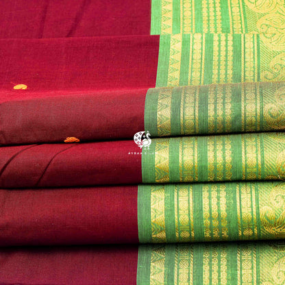 Folded maroon cotton saree showing the green zari border with mankolam paisley