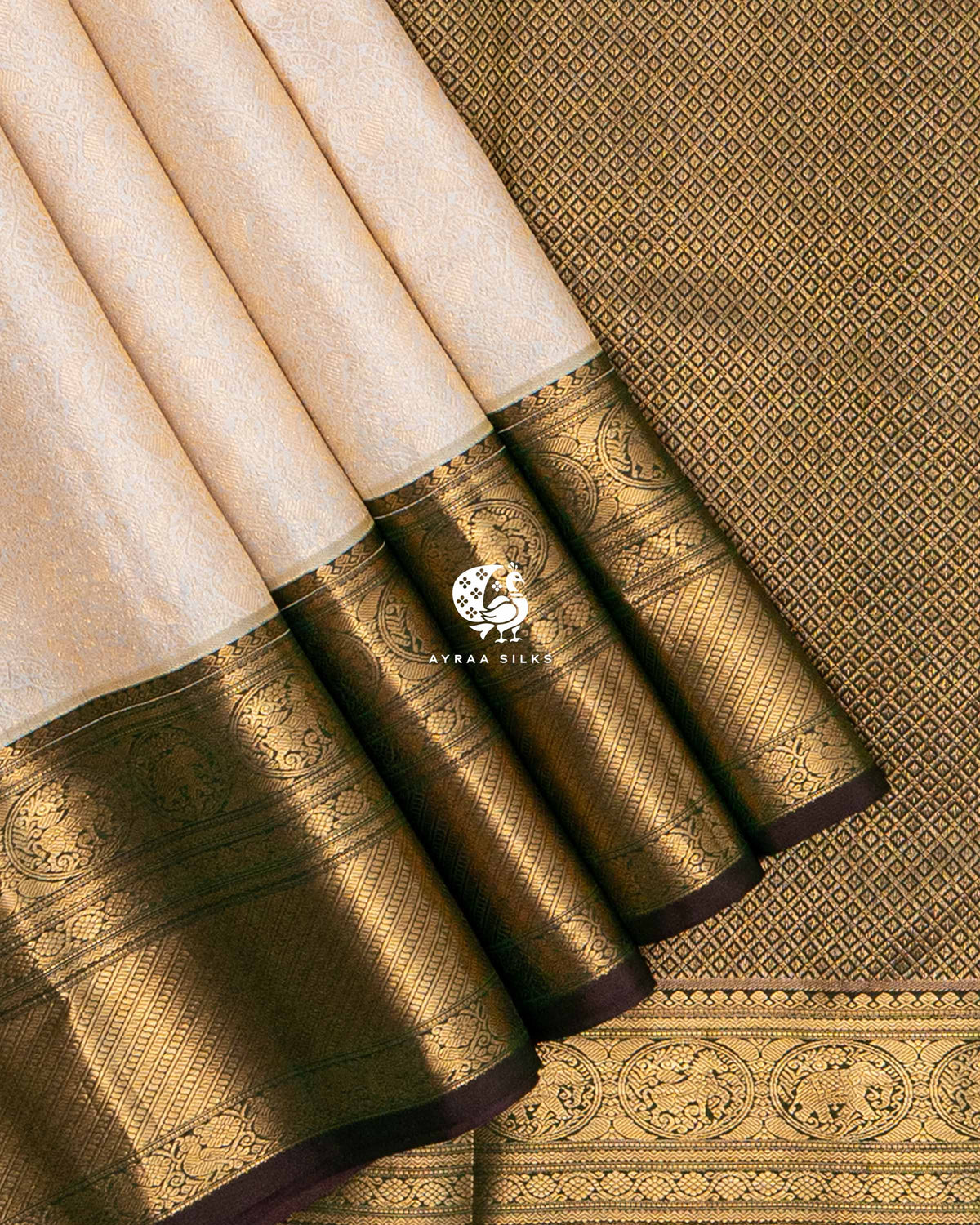 Close view of the Yanai (elephant) and Mayil (peacock) zari medallion border on cream pleats against the gold zari pallu