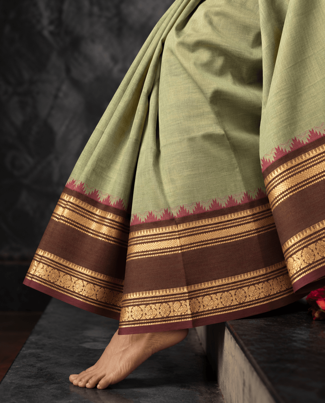 Woman wearing the pista green Kanchi cotton saree, draped to show the brown temple border with gold zari and maroon temple points