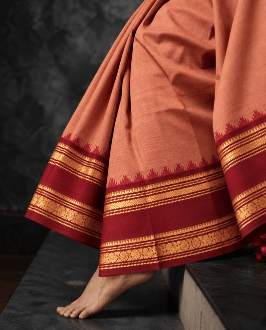 Woman wearing the peach Kanchi cotton saree, draped to show the brick red temple border with gold zari